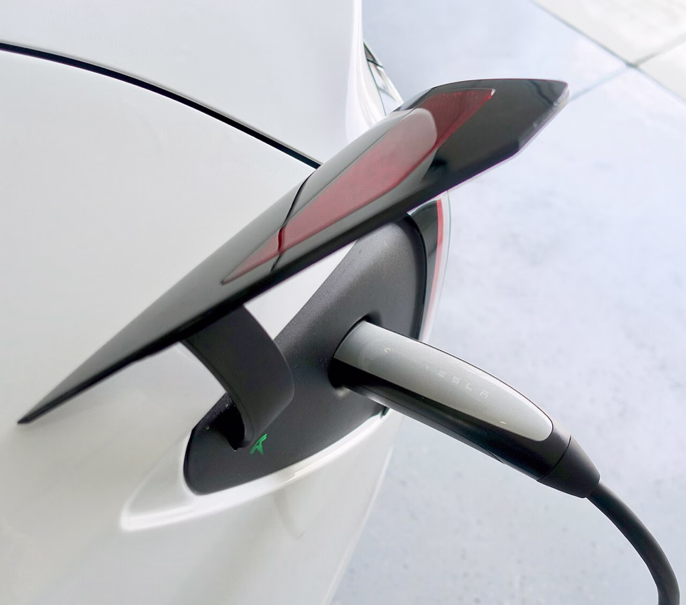 Ein ladender Tesla mit dem schlanken NACS-Stecker